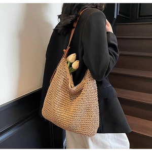 Straw hobo shoulder bag with leather strap worn by a model in a minimalist urban setting