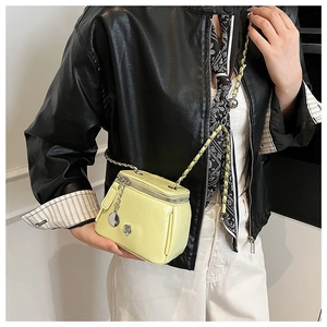 Detail of yellow mini square crossbody bag featuring silver chain strap and flower emblem