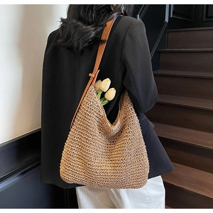 Detail of hand-woven straw tote bag with brown leather strap on a model's shoulder