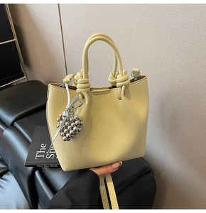 Detail of light yellow lychee leather bucket bag with knot handle and heart charm