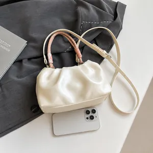Detail of cream pleated cloud bag with pink braided handle and crossbody strap next to phone