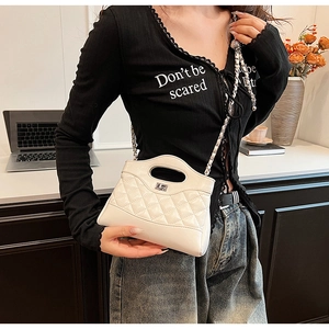 Detailed view of white quilted chain handbag with metal turn-lock on a stylish model