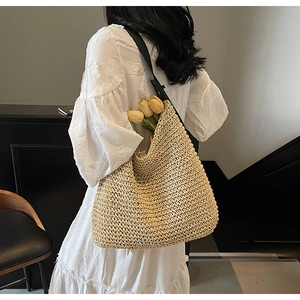 Detail of a beige woven straw tote bag with black faux leather strap and decorative tulips
