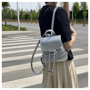 Nahaufnahme eines silbernen Mini-Rucksacks mit Faltenstruktur und Metallplakette-Detail