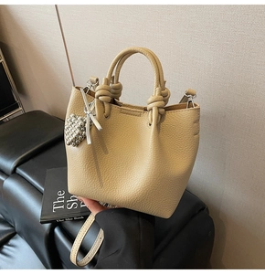 Close-up of beige lychee grain leather bucket bag with knotted handle and silver bead charm