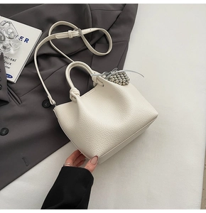Detailed shot of beige lychee grain bucket bag with pearl pendant on a grey blazer