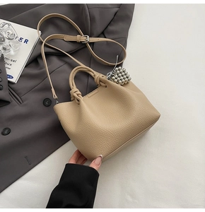 Detail view of beige lychee leather bucket bag featuring a unique knot handle and silver charm