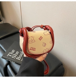 Détail d'un mini sac selle en cuir beige avec garniture rouge et imprimé d'oursons