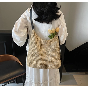 Detailed texture of hand-woven straw tote bag with black leather strap and floral decor
