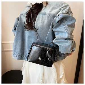 Detail of black glossy crossbody bag with silver flower accent and metal chain strap