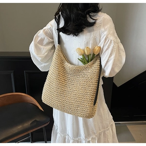 Detail of a large straw woven shoulder bag with black leather straps and tulip decor