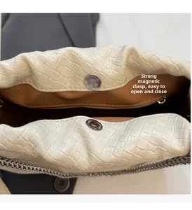 Detail of the magnetic buckle closure and chain trim on the beige woven bucket bag