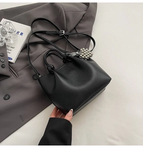 Close-up of black lychee grain leather bucket bag with elegant pearl charm accessory