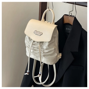 Detail eines cremefarbenen Falten-Mini-Rucksacks mit Fashion-Logo vor schwarzem Blazer