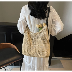 Detail of hand-woven straw shoulder bag with black leather strap and floral accents