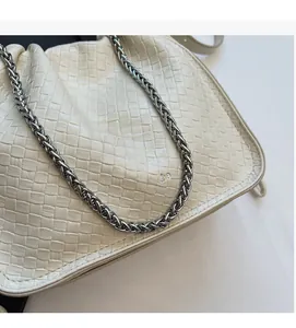 Detailed macro view of woven leather texture and silver chain strap on cream bucket bag