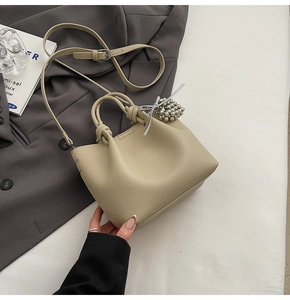 Detail of beige lychee grain leather bucket bag with silver charm on grey suit background