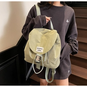 Detail of light green drawstring backpack featuring a metal buckle and woven label