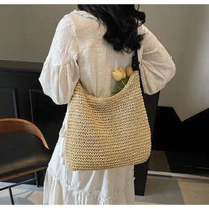 Detail of hollow straw shoulder bag with black strap worn over a white lace dress