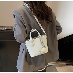 Detail of light green bucket bag with silver heart charm on grey blazer outfit