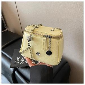 Détail du sac bandoulière jaune en forme de boîte avec chaîne et pendentif fleur