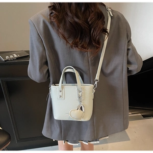 Close-up of a grey litchi grain bucket bag with a heart charm shown in a crossbody style