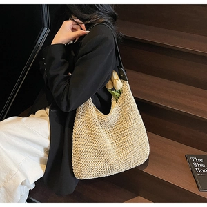 Detail of a beige woven hobo bag with black leather strap on a model on wooden stairs