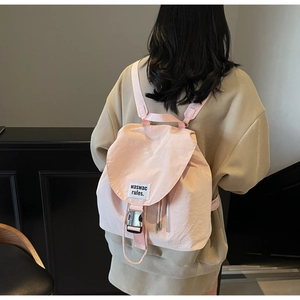 Detail of pink drawstring backpack featuring white letter patch and silver metal buckle