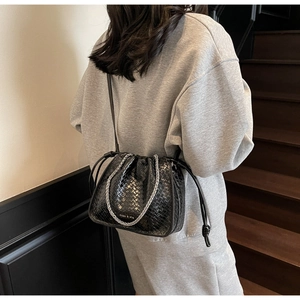 Detail of black woven bucket bag showing textured synthetic leather and silver chain strap