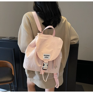 Detail of light pink nylon backpack featuring metal buckle closure and white logo patch