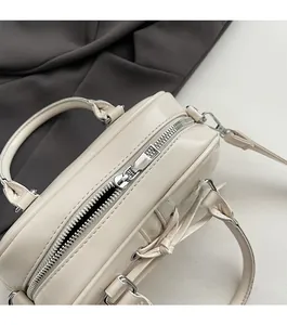 Dettaglio delle doppie cerniere in metallo argentato sulla borsa bauletto in ecopelle crema