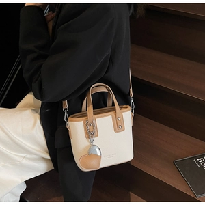 Detail of cream bucket bag with brown trim and heart charm on a wooden background