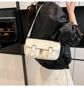 Detail of cream shoulder bag featuring double front flap pockets and silver buckles on a model