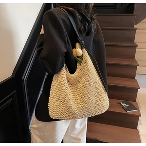 Detail shot of hollow straw woven tote with black shoulder straps on a casual model