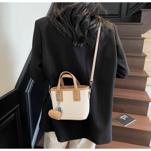 Detail of a two-tone bucket bag with heart charm shown on a professional outfit