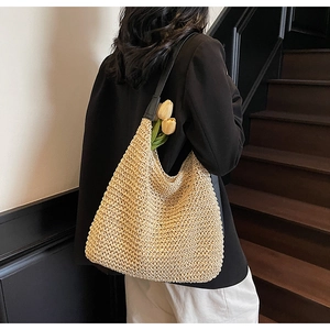 Detail showing handwoven beige straw tote bag with black leather straps on shoulder