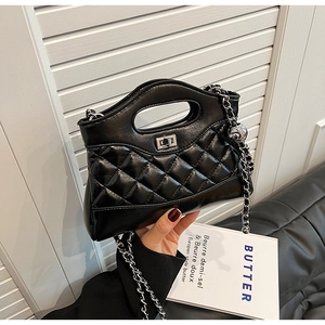 Detail of black quilted leather bucket bag with silver chain strap and metal charm