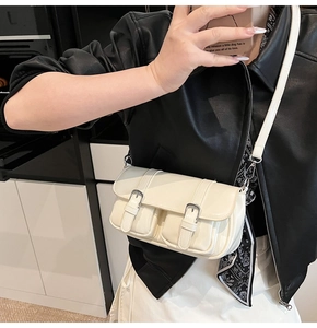 Close-up of beige faux leather baguette bag with dual buckle details and silver hardware