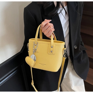 Detail of yellow bucket bag with silver chain, heart charm, and adjustable shoulder strap