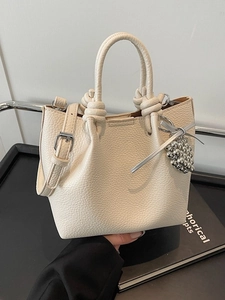 Elegant cream bucket bag with twisted handle and beaded grape charm on dark display