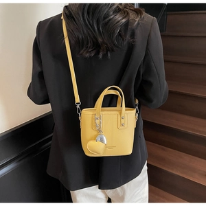 Close-up of yellow leather bucket bag featuring a gold heart charm and crossbody strap