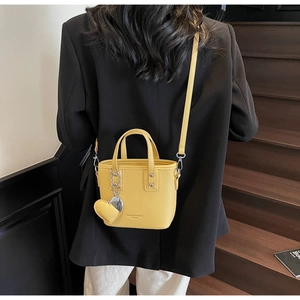 Detail of bright yellow bucket bag in lychee leather with heart charm and metal strap