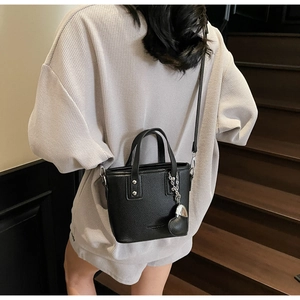 Detail of black pebbled leather mini bucket bag with heart charm on a wooden staircase