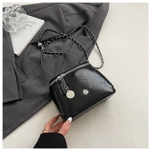 Detail of a black glossy crossbody bag featuring a silver chain and camellia flower charm