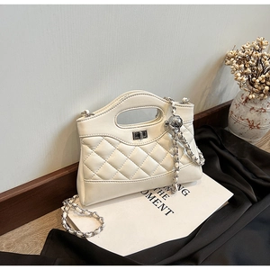 Close-up of white quilted chain handbag with silver turn-lock on minimalist books