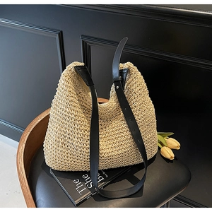 Detail of hand-woven straw bag texture and adjustable black leather shoulder strap