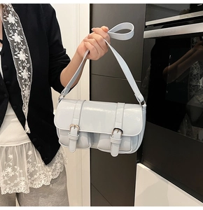 Close-up of light blue glossy patent leather shoulder bag with double buckle straps
