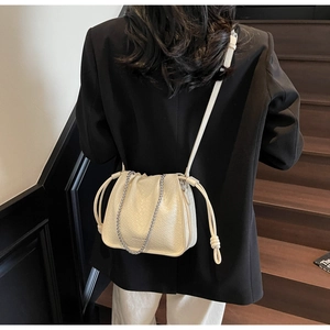 Detail of off-white crocodile embossed bucket bag with silver chain strap on model