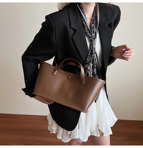 Detail of dark brown leather tote bag held by a model in elegant professional attire