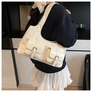 Detail view of cream white patent leather tote bag with dual pockets and silver buckles
